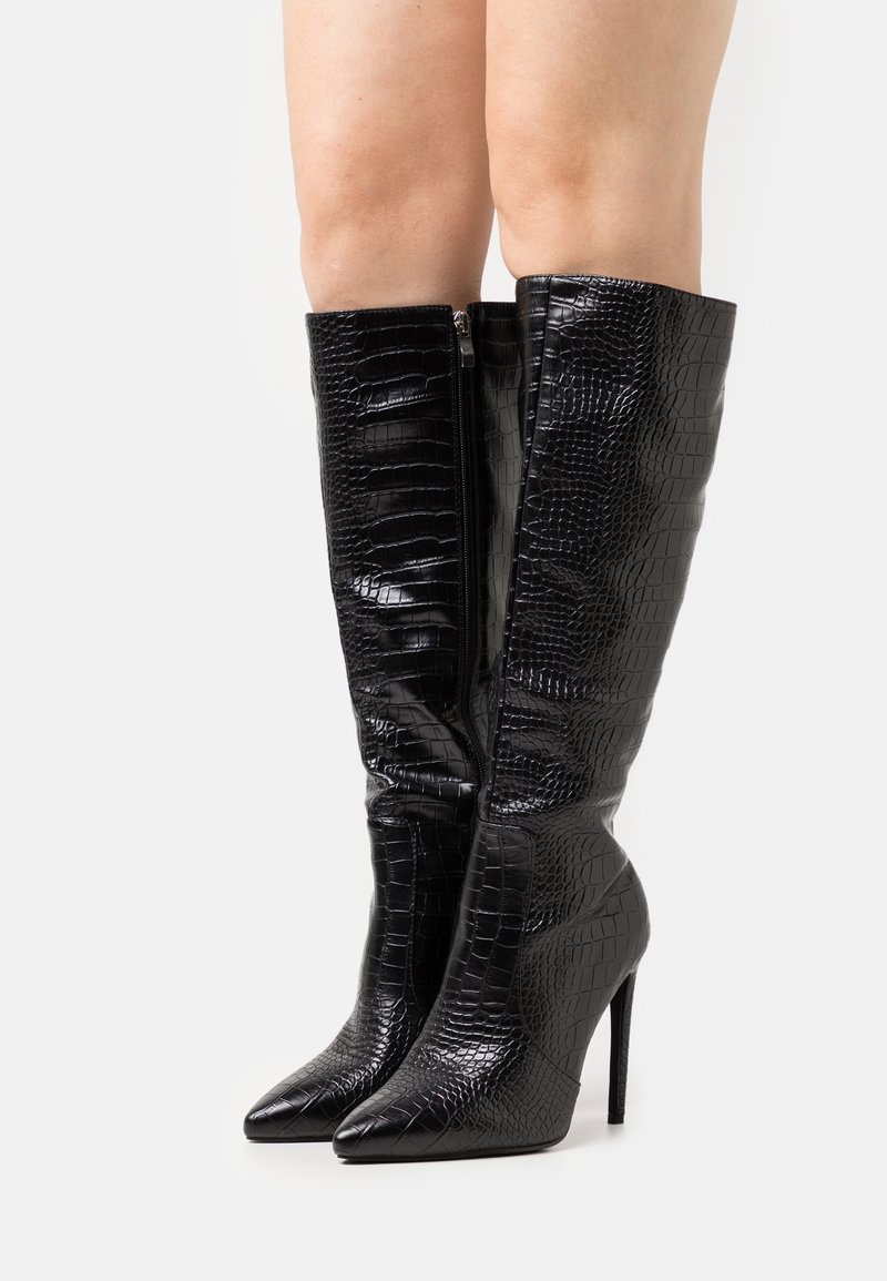 Bottes noires arrivant au genou avec une texture gaufrée crocodile, bout pointu, talon aiguille et une fermeture éclair sur le côté pour un enfilage facile.