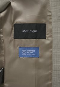 Wnętrze garnituru Matinique z czarną metką marki oraz niebieską metką pielęgnacyjną nadającą się do prania w pralce, z ikoną pralki.