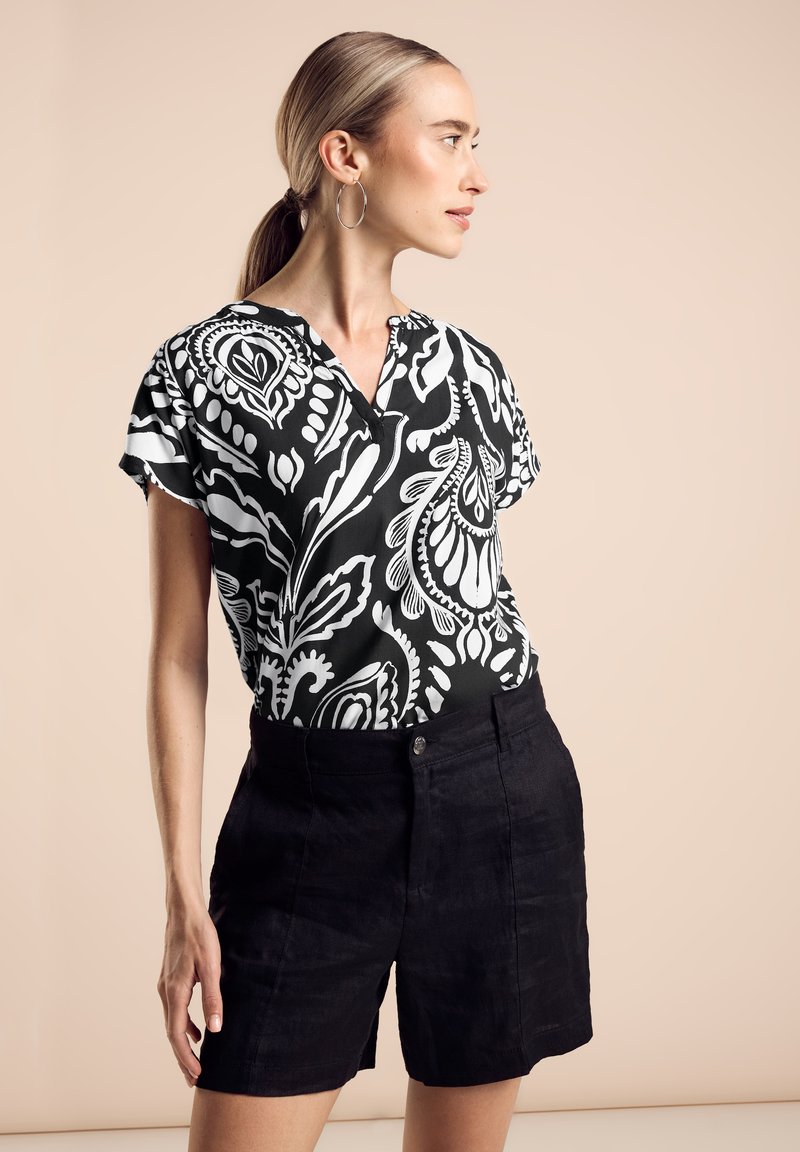 Blusa a maniche corte a motivi bianco e nero con scollo a V, abbinata a pantaloni corti neri in lino a vita alta. Tessuto dalla consistenza liscia.
