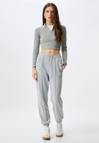 Grijs cropped longsleeve shirt met een rits-kraag, gecombineerd met loszittende grijze sweatpants met een elasische tailleband en boordjes aan de zoom.