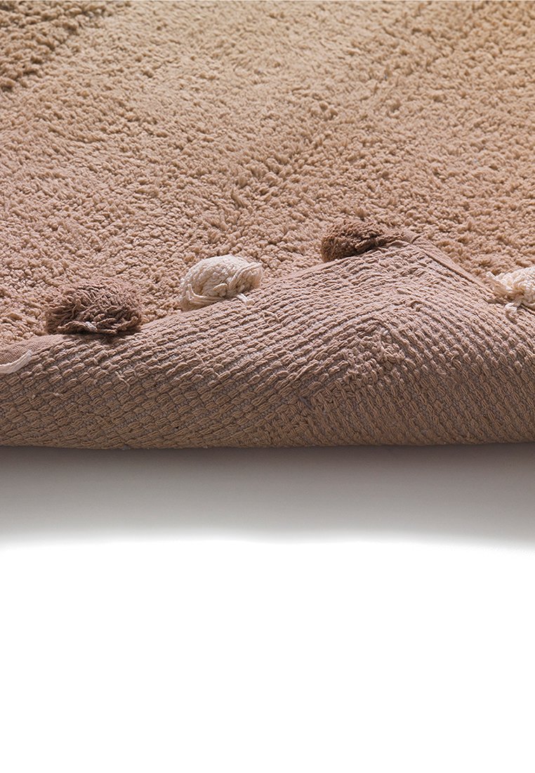 Dywan o fakturze beżowej z puszystą powierzchnią, udekorowany trzema pomponami w różnych odcieniach brązu i kremu wzdłuż krawędzi.