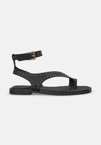 Chanclas planas negras con un diseño de tira en T, acentos de tachuelas, hebilla ajustable en el tobillo y una suela de textura suave.