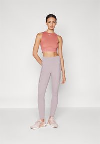 Haut de sport cropped rose avec un logo, assorti à un legging taille haute violet clair avec des poches zippées sur les côtés, et des chaussures de sport rose clair.
