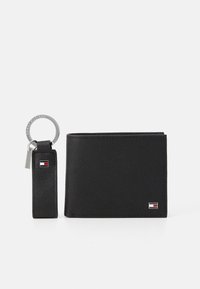 Portefeuille en cuir noir avec une texture et un porte-clés. Présente un petit emblème et un anneau de clé attaché par une sangle. Design compact.