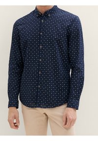 Camisa de botones azul marino en tela ligera con un patrón geométrico blanco, cuello puntiagudo y botones marrones en contraste. Mangas largas.
