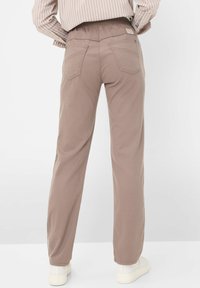 Pantaloni dritti di un marrone chiaro, con una cintura elastica, tasche posteriori e una superficie liscia. Indossati con sneakers bianche.