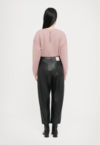 Roze oversized sweatshirt met een ritsdetail aan de achterkant, gecombineerd met zwarte leren broek met hoge taille en zwarte haklaarzen.