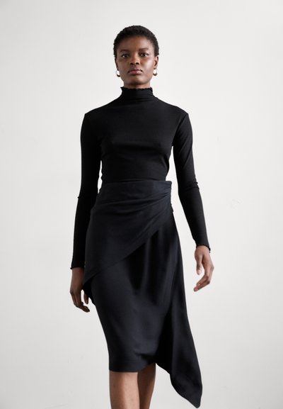Top nero a maniche lunghe con collo alto, abbinato a una gonna nera elegante con un design drappeggiato asimmetrico. Tessuto dalla texture morbida.