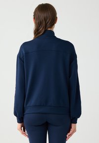 Felpa blu navy con colletto alto, maniche lunghe e polsini elasticizzati. Tessuto morbido con una texture liscia. Design semplice, senza motivi.