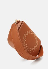Borsa in finta pelle marrone con logo borchiato in tonalità oro, forma arrotondata e tracolla in tessuto con nome del marchio impresso. Chiusura superiore con zip.