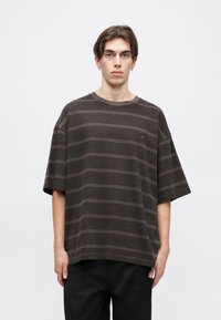 Camiseta oversized de rayas marrones hecha de una tela suave. Presenta un cuello redondo y mangas cortas con una sutil textura en las rayas.