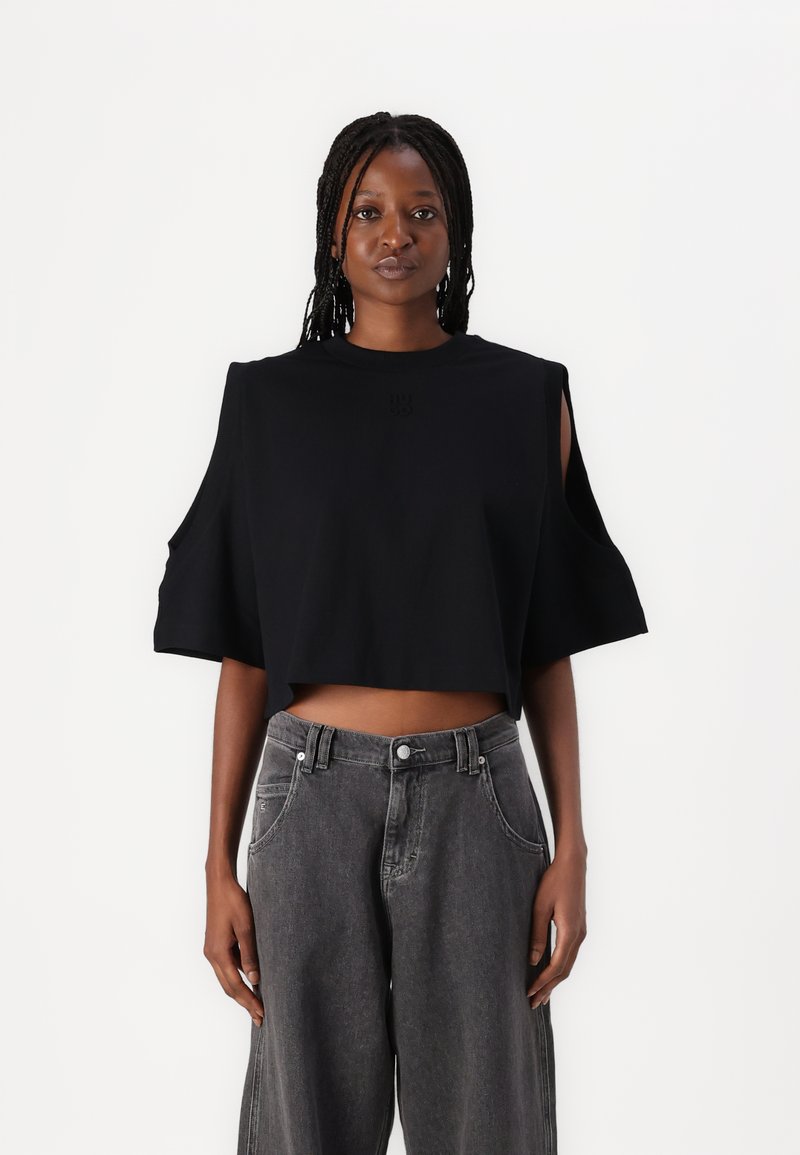 Camiseta negra corta con mangas cortas, con hombros descubiertos y una textura suave. Combinada con unos vaqueros grises de cintura alta.