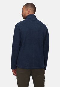 Navy fleece jacket with a high collar, textured surface, and subtle branding at the back. Features elastic cuffs and hem.