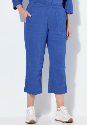 Pantalones recortados azules de tela texturizada con una cinturilla elástica, que cuentan con bolsillos laterales. Combinados con zapatillas blancas.