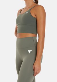 Sujetador deportivo verde oliva con tirantes finos y un diseño ajustado. Leggings verde oliva de talle alto con un sutil logo en blanco.