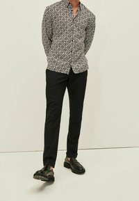 Camisa de patrón en blanco y negro con diseños geométricos, combinada con pantalones negros ajustados y zapatos negros brillantes.