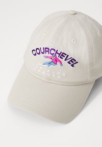Beige baseballcaps med brodert "Courchevel"-tekst, skikjører grafikk i rosa og blått, og hvit skrift for "THE ALPS FRANCE."
