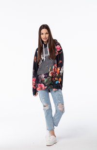 Sudadera con base negra, con vibrantes patrones florales y rayas abstractas. Combinada con jeans claros desgastados y zapatillas blancas.