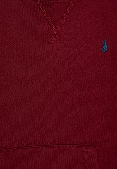 Sudadera color marrón con una superficie texturizada, que presenta un logotipo azul bordado en el pecho y costuras reforzadas alrededor del escote.