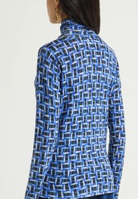 Maglia a maniche lunghe blu con motivo geometrico in nero e bianco. Presenta un collo alto e una forma aderente. Tessuto dalla texture liscia.