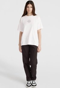 Hvid bomulds t-shirt med et cirkulært logo centreret på brystet, parret med sorte cargo bukser og sorte-hvide sneakers.