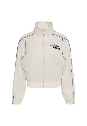 Veste courte beige clair à col montant, fermeture éclair devant, ourlet et poignets élastiques, passepoil noir et logo "Calvin Klein" sur la poitrine gauche.