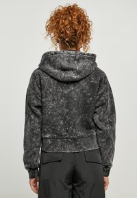 Sudadera negra recortada con una textura desgastada, que cuenta con capucha ajustable y puños acanalados. Diseño simple con detalles de costura visibles.