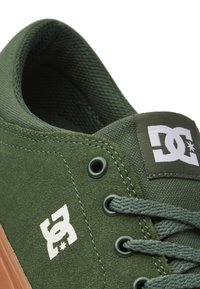 Gröna mockaskate skor med en texturerad yta, utrustade med metallöglor, gröna snören och en vit logopatch på tungan.