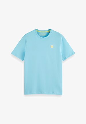 Helles blaues T-Shirt mit kurzen Ärmeln aus weicher Baumwolle, das auf der linken Brustseite ein kleines gelbes Logo-Patch aufweist. Schlichtes Rundhalsdesign.