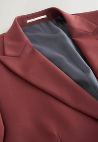Bordó blézer zakó sima textúrával, strukturált hajtókákkal és szürke szatén béléssel. Tiszta, szabott kialakítással rendelkezik, látható záródások nélkül.