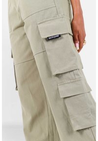 Cargo broek in lichtbeige stof met meerdere zakken, een stevige ontwerp en een zichtbaar merklogo op de zijkant.
