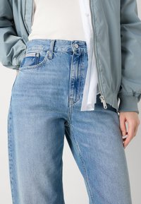 Svijetloplave traperice viskog struka u opuštenom kroju s blagim izbljeđivanjem, s logom Calvin Klein na pojasu i klasičnim dizajnom s pet džepova.
