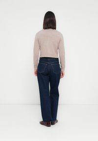 Suéter cropped beige, jeans de pierna ancha azul oscuro, textura suave, diseño sencillo, con cuatro bolsillos y zapatos oscuros.
