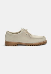 Pantofle bej din suede cu un panou frontal texturat și striat și o talpă din cauciuc de culoare maro deschis. Prezintă un design cu șireturi și vârf rotund.