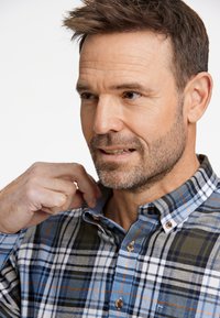 Camisa de cuadros de botones en azul, blanco, verde y naranja. Presenta un patrón de pata de gallo, collar y botones de madera. Tejido texturizado.