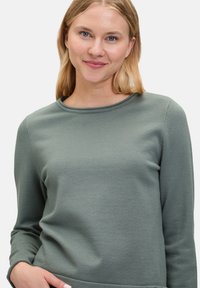 Hellgrüner Langarm-Pullover mit Rundhalsausschnitt und gerippter Textur. Taillierte Passform mit Nahtdetails entlang der Ärmel.