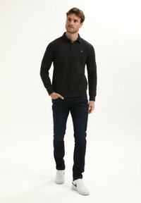 Zwarte lange mouw polo met een klein logo, gecombineerd met donkerblauwe jeans en witte sneakers, met een eenvoudig, strak ontwerp.