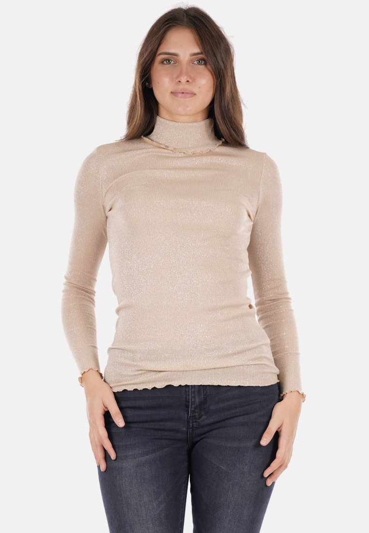 Maglione beige a maniche lunghe con collo a bottleneck, caratterizzato da una texture a coste e un leggero luccichio, con un orlo ondulato e una silhouette aderente. Indossato con jeans scuri.