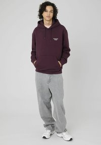 Sweat à capuche bordeaux avec une poche avant et le texte blanc « Create Your World ». Associé à un pantalon ample gris clair et des baskets blanches.