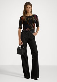 Top negru cu model, cu mâneci scurte, având detalii din lanț aurit; asortat cu pantaloni evazați din denim închis cu talie înaltă și o geantă mică neagră.
