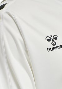 Hvid sports trøje lavet af glat stof med et sort logo, med kontrasterende striber på skuldrene. Skræddersyet design til atletisk pasform.