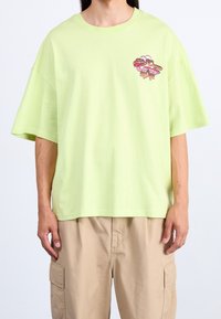 Hellgrünes, oversized T-Shirt aus Baumwolle mit einem gedruckten Design und dem Text "Ice Cream Candy" auf der linken Brustseite. Kurzärmlig.