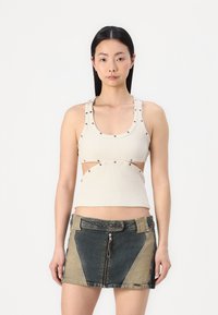 Top in maglia beige a coste con ritagli e dettagli decorativi a pressione, abbinato a una mini gonna in denim con pannelli in tessuto a contrasto e cerniera frontale.