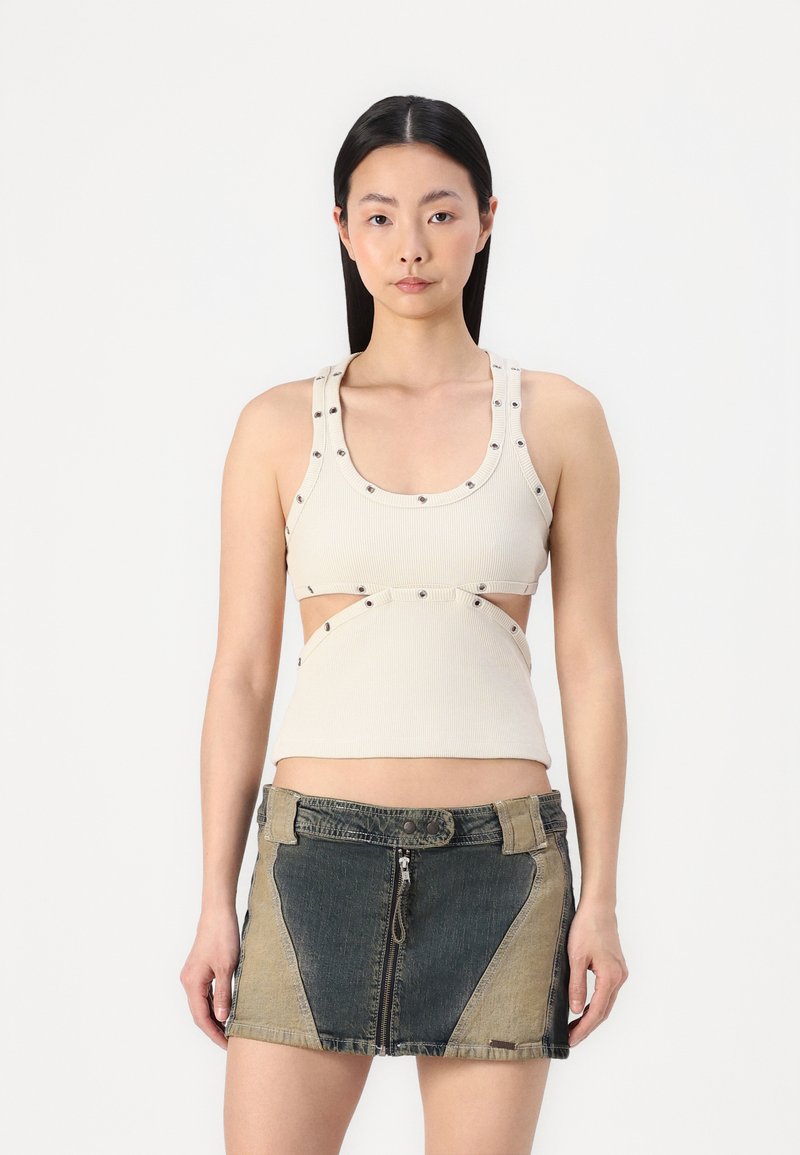 Top in maglia beige a coste con ritagli e dettagli decorativi a pressione, abbinato a una mini gonna in denim con pannelli in tessuto a contrasto e cerniera frontale.