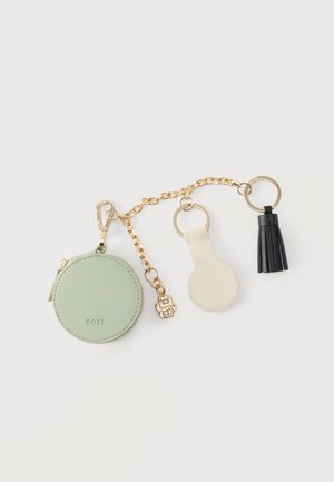 Porte-monnaie rond vert, porte-clés rond en cuir beige et pompon en cuir noir attachés par une chaîne dorée avec des anneaux.