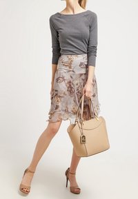 Vaaleanharmaa pitkähihainen yläosa, kukkakuvioinen läpikuultava hame, beige käsilaukku kultaisella nimikekilvellä ja vaaleanruskeat korkokengät.