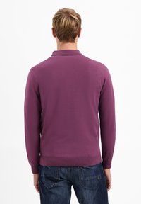 Paarse langemouwen polo-shirt met een gebreide textuur, voorzien van een kraag en geribde manchetten, gedragen met een blauwe spijkerbroek, van achteren getoond.