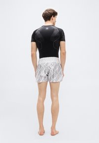 Μαύρο κοντομάνικο κορμάκι με υφή πάνελ και στρογγυλό λογότυπο, σε συνδυασμό με ανοιχτό γκρι σορτς που διαθέτουν επαναλαμβανόμενο μοτίβο λογότυπων και ελαστική μέση.