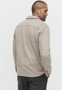 Beige ulljacka med krage, långa ärmar och knappdetalj vid manschetterna. Slät textur och skräddarsydd passform.