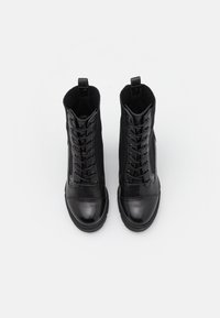 Bottes basses noires avec un bout en cuir lisse et une tige en tissu texturé, dotées d'une fermeture à lacets et d'une languette à l'arrière.